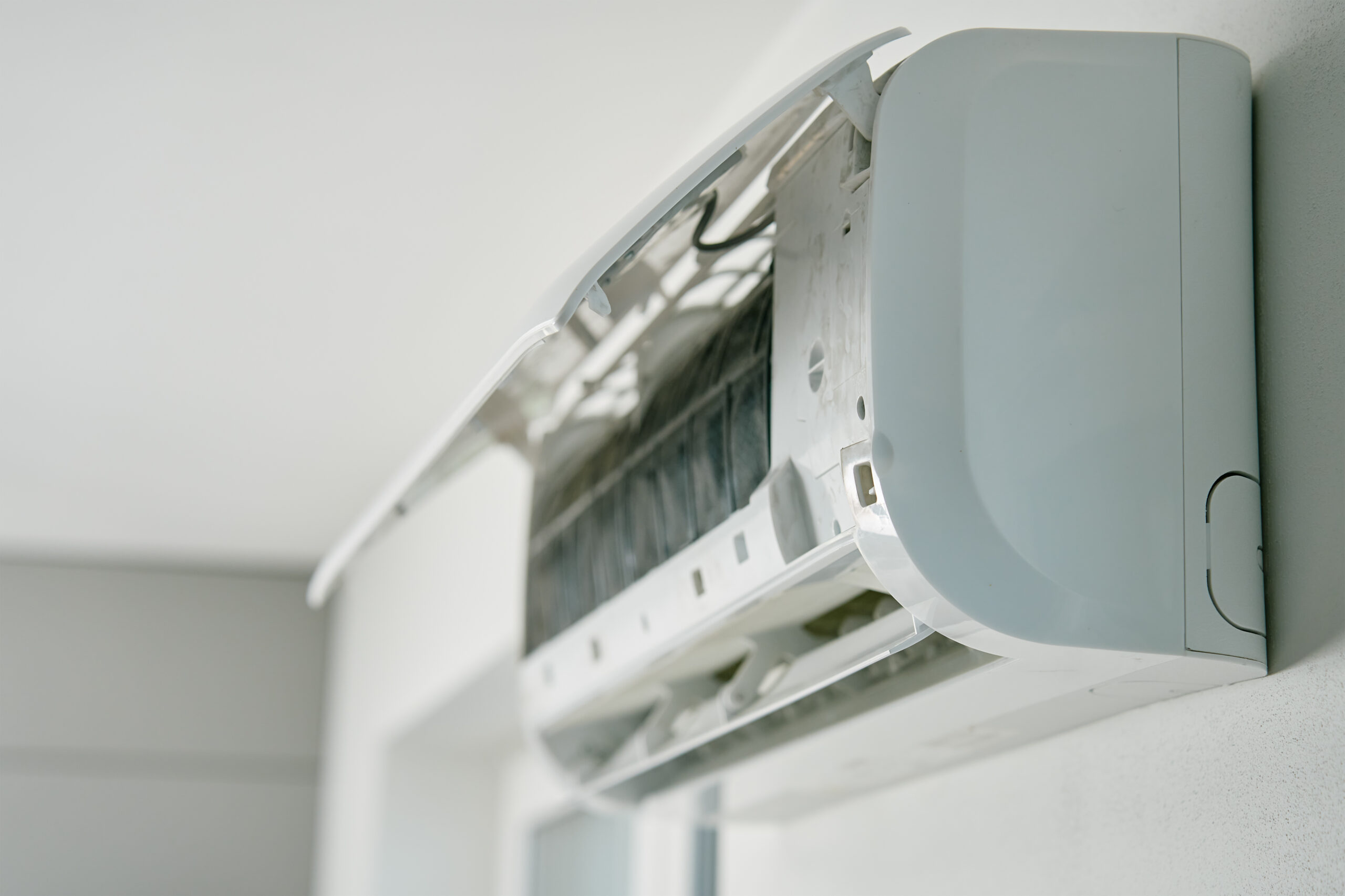 White air conditioner unit is mounted on wall, ready for maintenance. Climate system with opened front cover revealing internal components. Repairing HVAC in apartment